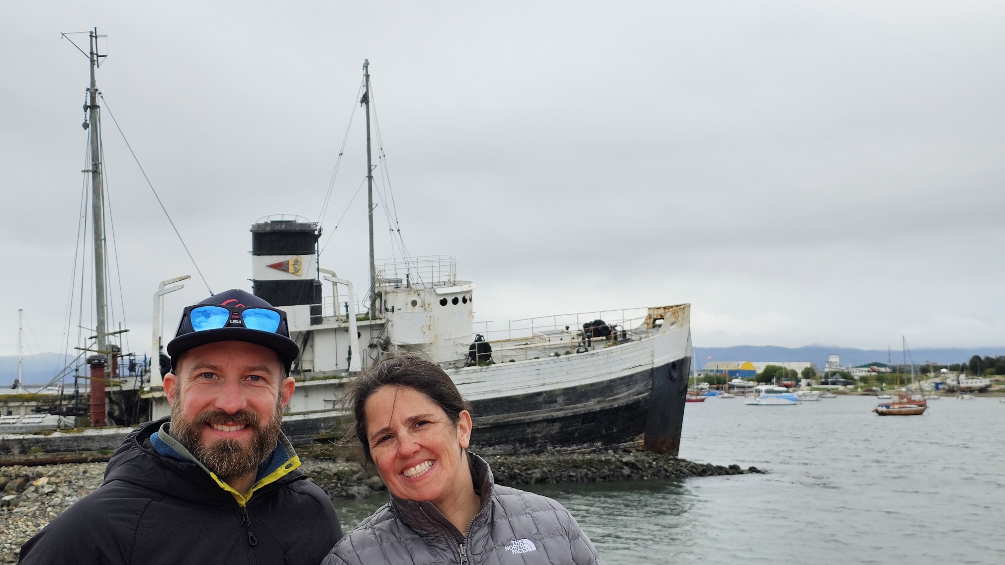 Brian and Jennifer Schwan on the Beagle Channel waterfront in Ushuaia, Argentina, with a rusted ship behind them