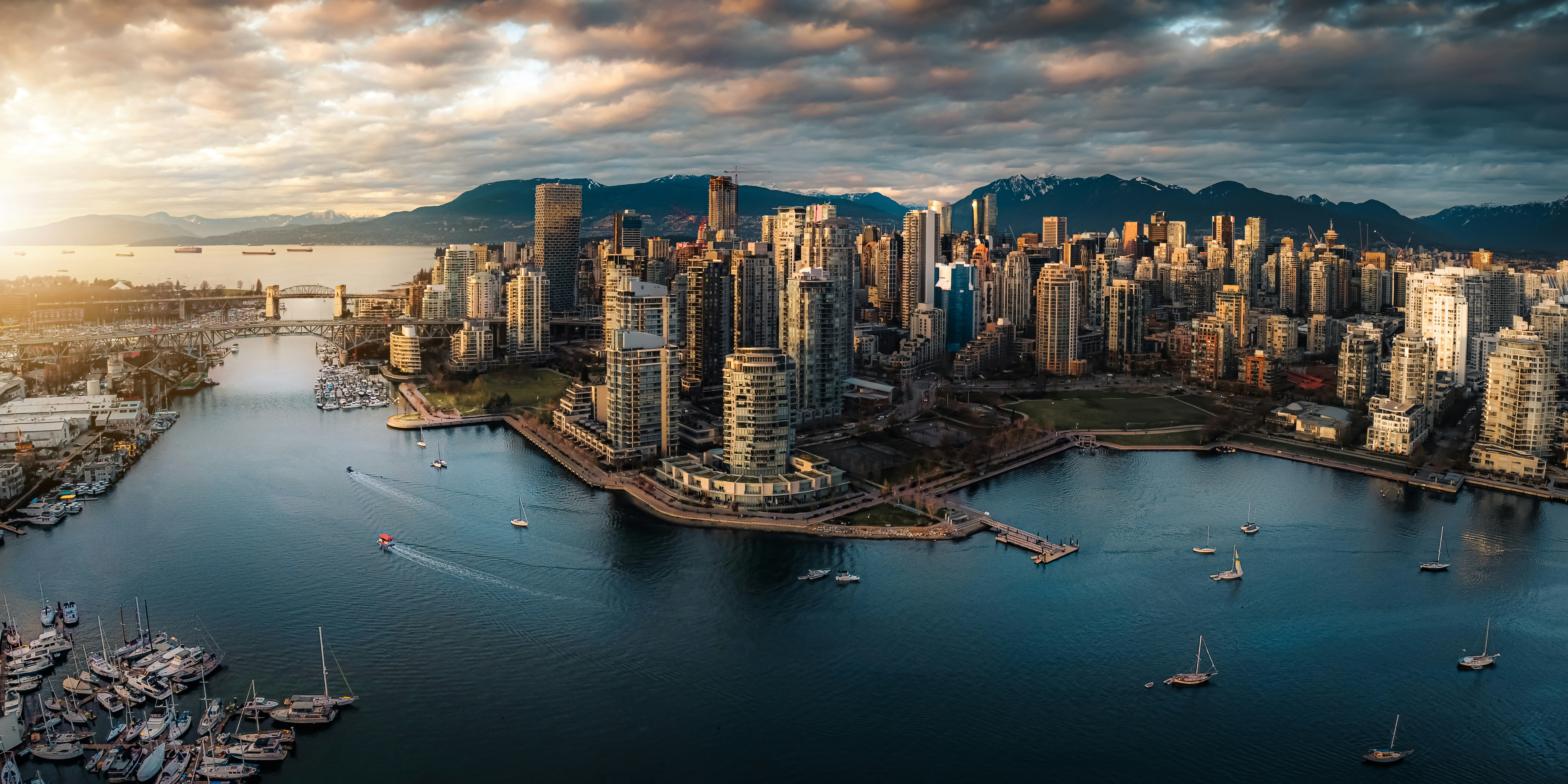 An aerial view of the Vancouver skyline at sunset, mountains rising behind the harbor
