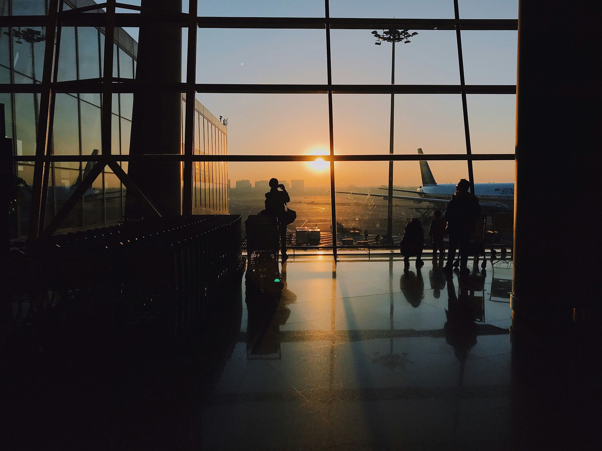 Silhouettes of travelers standing inside an airport terminal during golden hour
