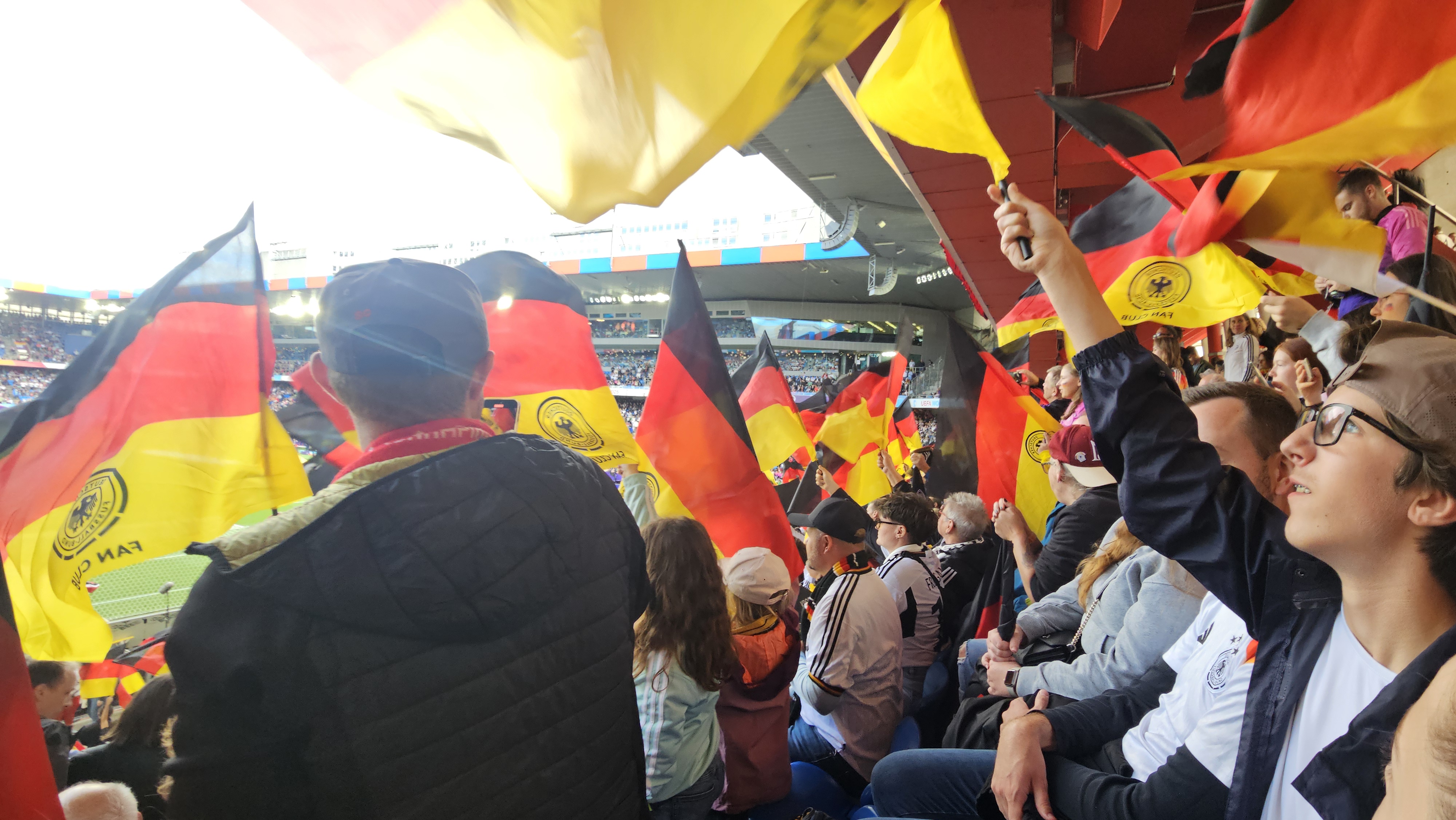 A young fan watching a soccer match in a European stadium, surrounded by supporters in team colors