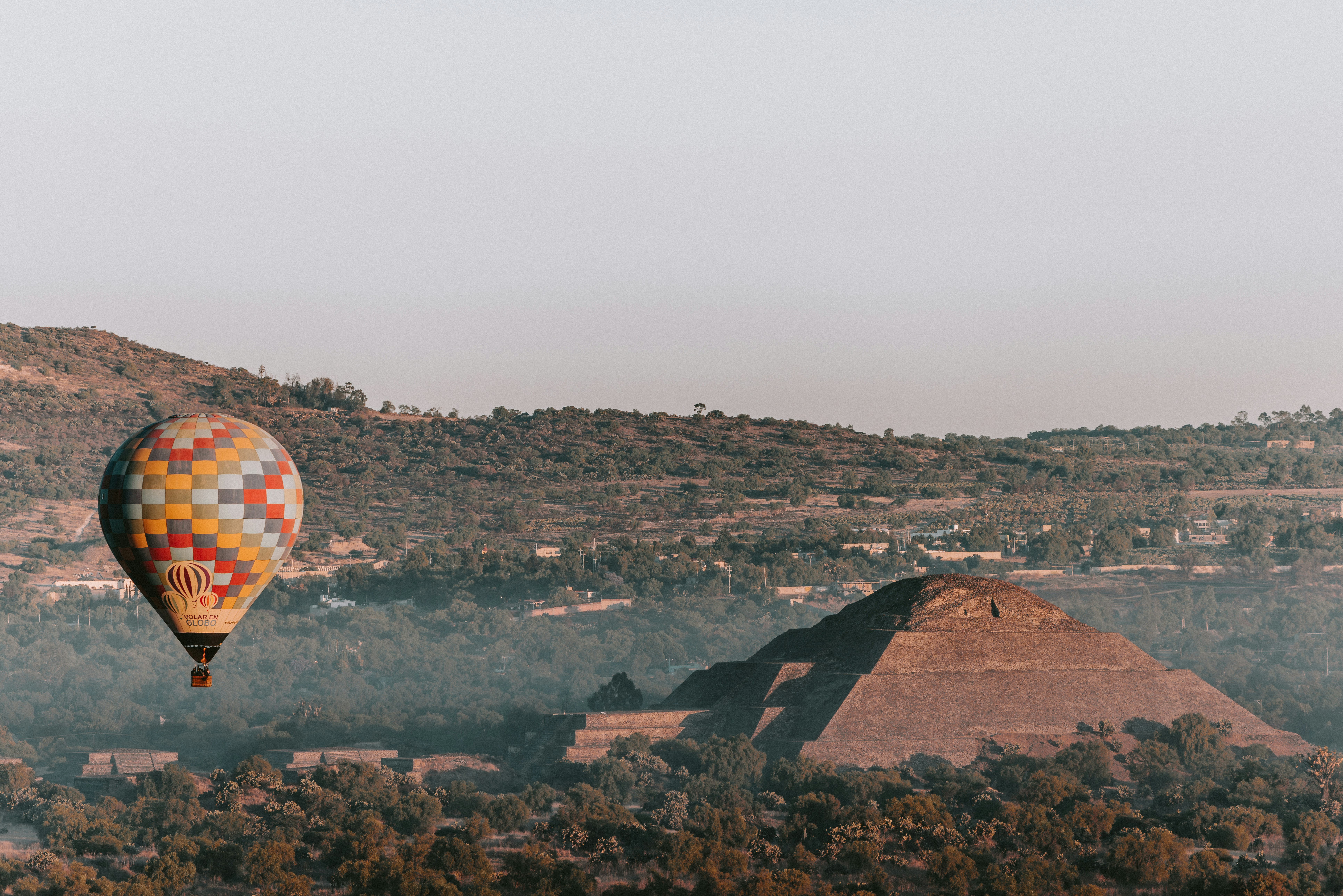 A hot air balloon floating over a pyramid in central Mexico at sunrise