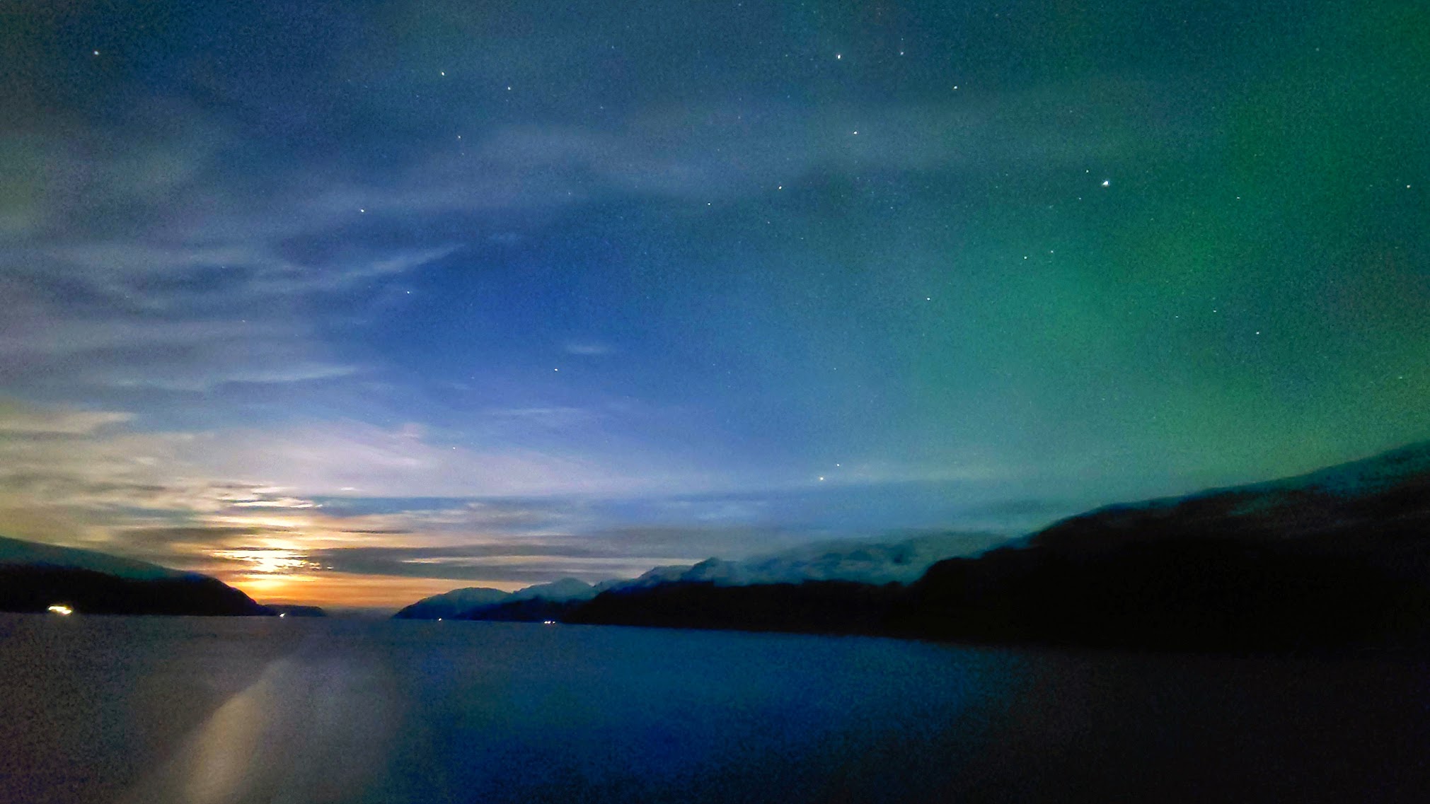 The Arctic sky at dusk in Norway, with the faint beginning of the Northern Lights over a still fjord