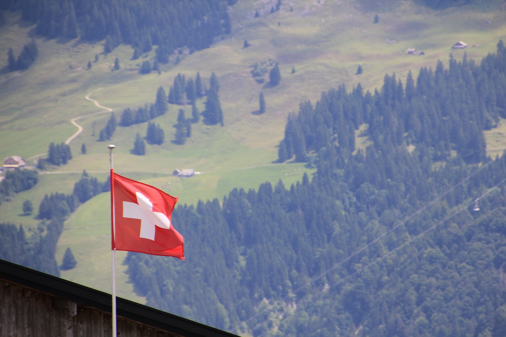 The Swiss flag flying against a backdrop of alpine peaks and blue sky
